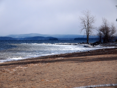 [Large expanse of sand with snowy, icy waters at the sand's edge. Hazy mountains seen in the distance.]